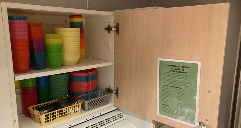 Olikfärgade muggar i ett skåp.
