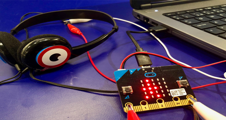 En microbit och hörlurar vid en dator.